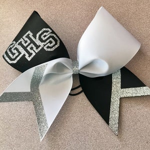 May include: Black and white cheer bow with silver glitter accents. The bow has the letters "GHS" in silver glitter on the black side.