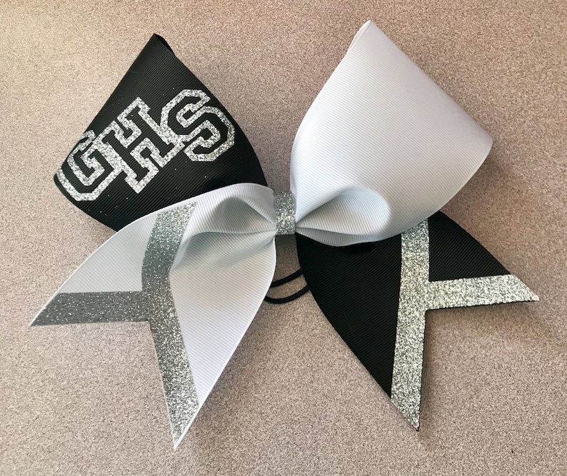 May include: Black and white cheer bow with silver glitter accents. The bow has the letters "GHS" in silver glitter on the black side.