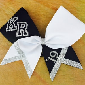 May include: Black and white cheer bow with silver glitter accents. The bow has the letters "KR" in silver glitter on the black side and the number "19" in silver glitter on the white side.