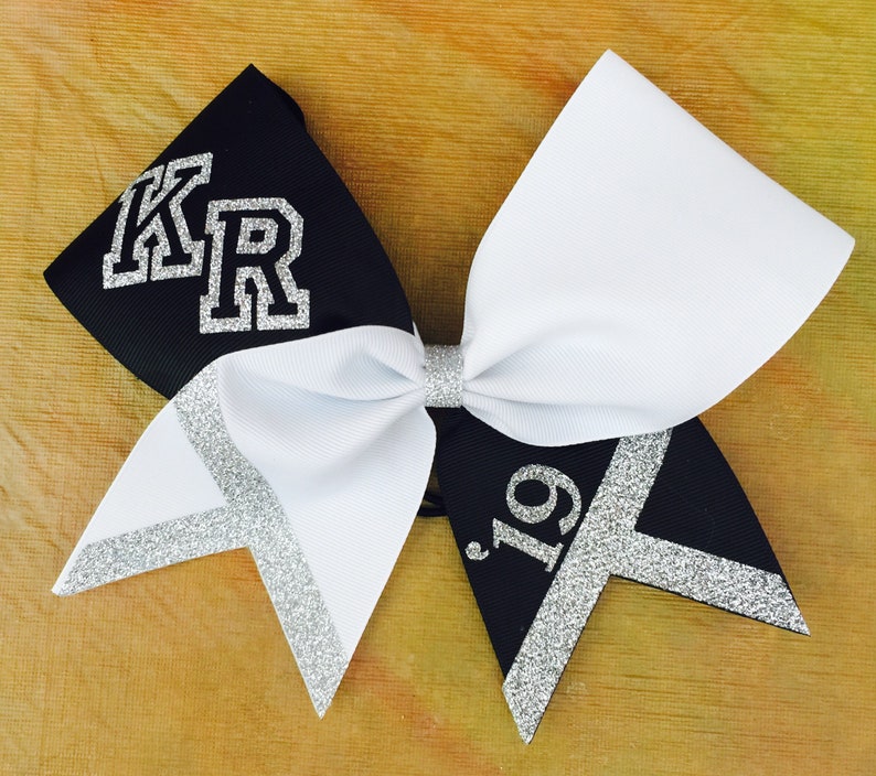 May include: Black and white cheer bow with silver glitter accents. The bow has the letters "KR" in silver glitter on the black side and the number "19" in silver glitter on the white side.