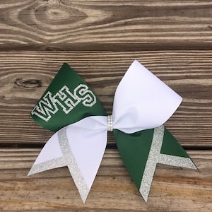 May include: A white and green cheer bow with silver glitter accents. The bow has the letters "WHS" in silver glitter on the green side.