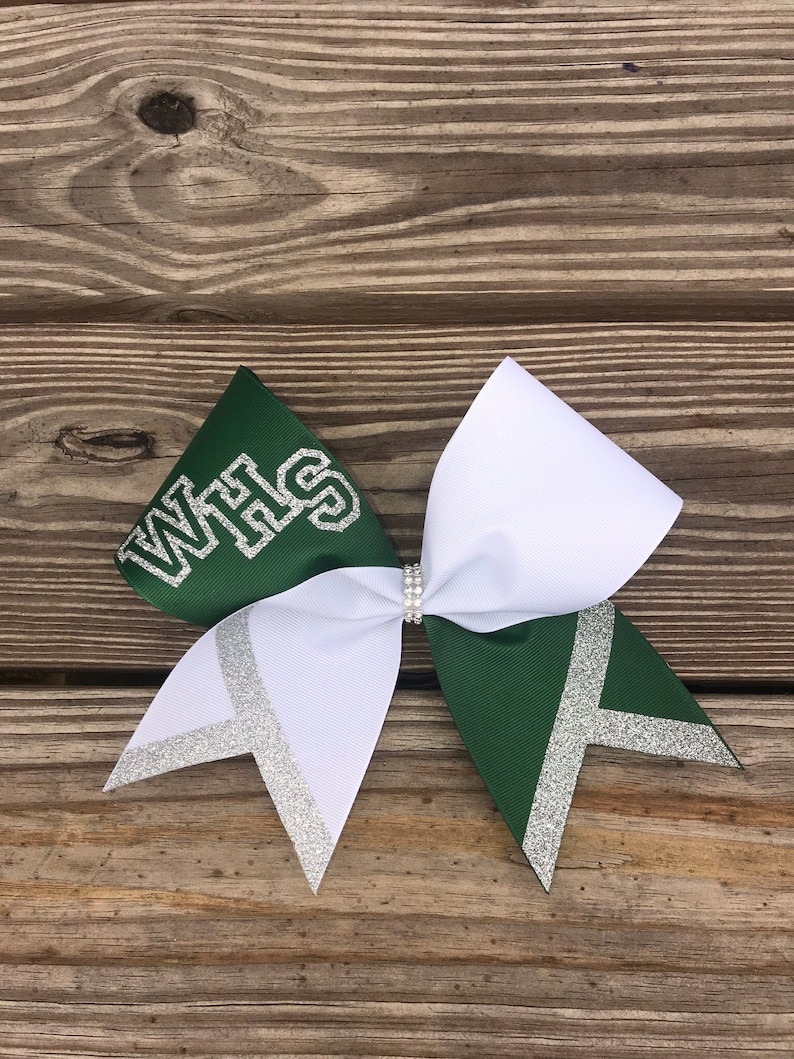 May include: A white and green cheer bow with silver glitter accents. The bow has the letters "WHS" in silver glitter on the green side.