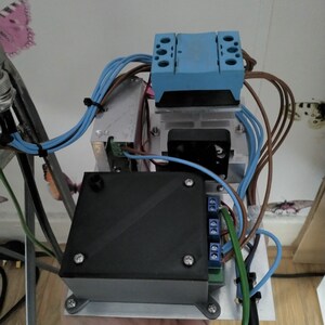 Może przedstawiać: Urządzenie elektroniczne z czarną obudową, niebieskim elementem i kolorowymi przewodami. Zamontowane na srebrnej metalowej podstawie, zawiera mały wentylator. Wymiary w centymetrach i gramach.