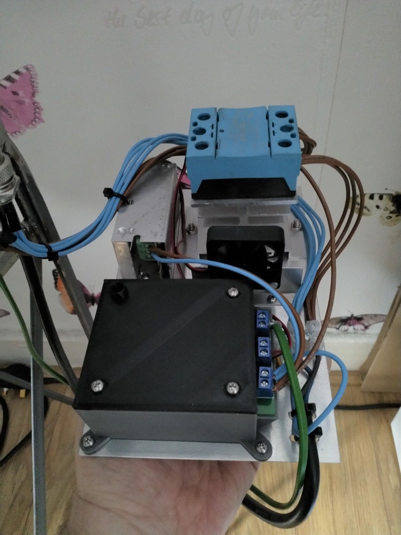 Może przedstawiać: Urządzenie elektroniczne z czarną obudową, niebieskim elementem i kolorowymi przewodami. Zamontowane na srebrnej metalowej podstawie, zawiera mały wentylator. Wymiary w centymetrach i gramach.