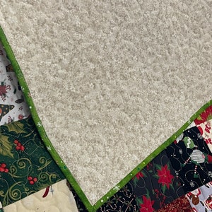 May include: A patchwork quilt with a variety of Christmas-themed patterns. The quilt features squares with images of Santa Claus, poinsettias, and gnomes. The quilt is trimmed with a green border.