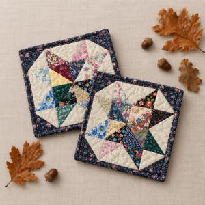 May include: Two square quilted coasters featuring a central star pattern made from various floral fabric patches in shades of blue, pink, yellow, and green, bordered by a dark blue floral fabric and cream-colored triangular accents.