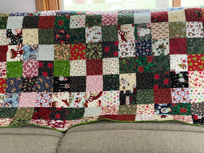 May include: A Christmas-themed patchwork quilt with a variety of festive patterns. The quilt features squares of red, green, white, and black fabrics, adorned with images of Santa Claus, snowmen, poinsettias, and candy canes. The quilt is edged with a green border.