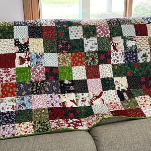 May include: A patchwork quilt with a Christmas theme, featuring squares of various festive patterns. The quilt showcases images of Santa Claus, snowflakes, and poinsettias in red, green, and white. The quilt is approximately 60 inches wide and 70 inches long.