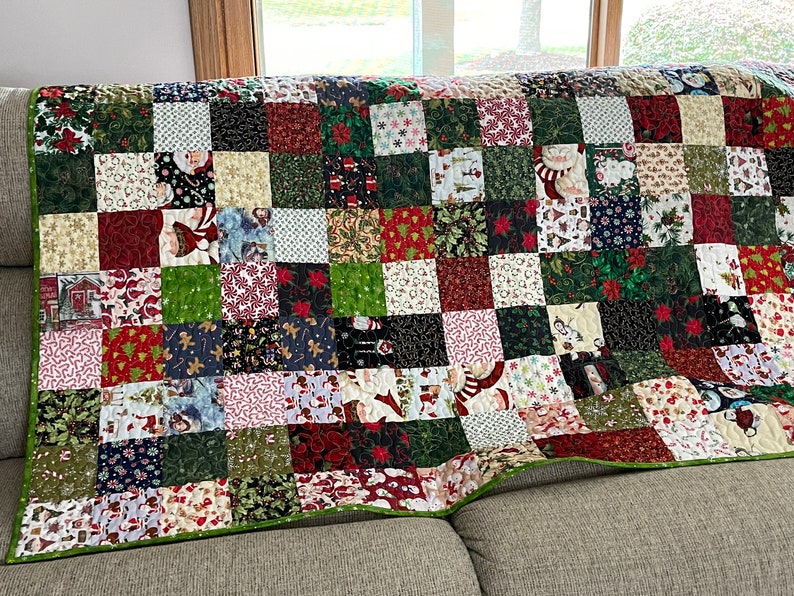 May include: A patchwork quilt with a Christmas theme, featuring squares of various festive patterns. The quilt showcases images of Santa Claus, snowflakes, and poinsettias in red, green, and white. The quilt is approximately 60 inches wide and 70 inches long.