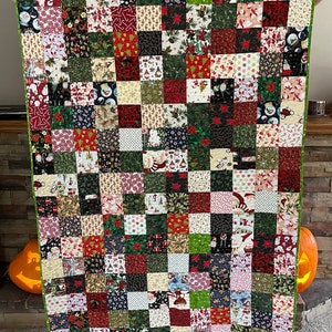 May include: A patchwork quilt with a green border, featuring a variety of Christmas-themed fabrics. The squares display patterns of Santa Claus, poinsettias, snowmen, and candy canes in red, green, white, and black.