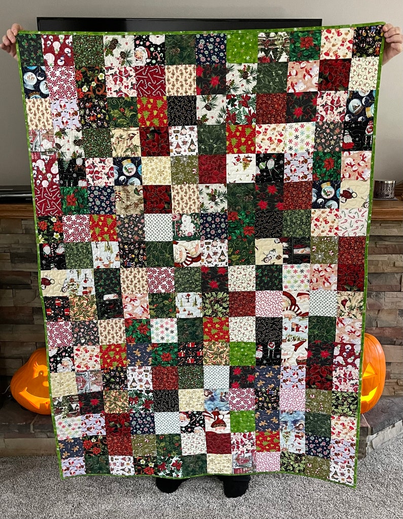 May include: A patchwork quilt with a green border, featuring a variety of Christmas-themed fabrics. The squares display patterns of Santa Claus, poinsettias, snowmen, and candy canes in red, green, white, and black.