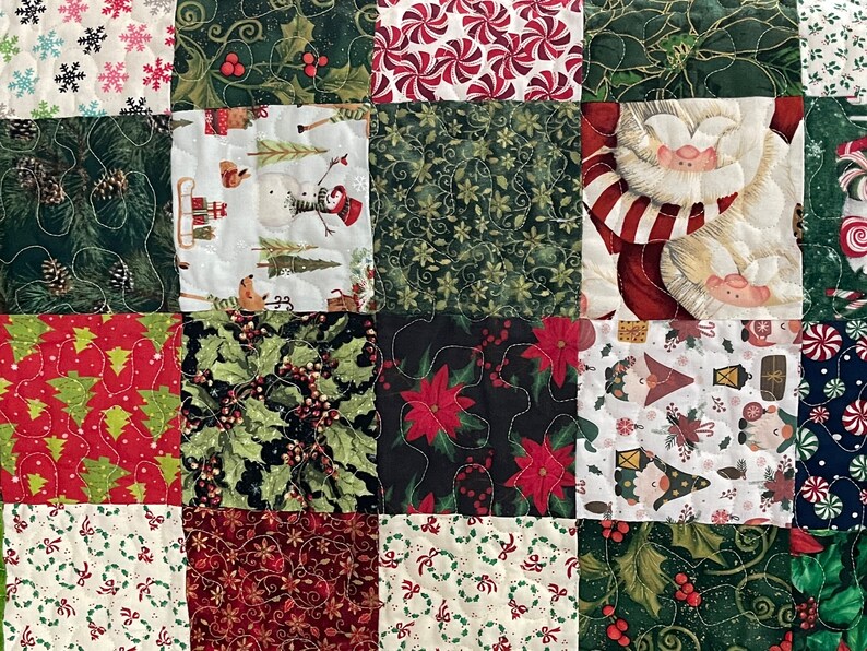 May include: A patchwork quilt with a festive Christmas theme. The quilt features various squares with holiday patterns, including snowflakes, holly, candy canes, snowmen, and Santa Claus. The colors are predominantly red, green, and white.