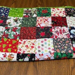 May include: A patchwork quilt with a green border, featuring various Christmas-themed fabrics. The squares display patterns of poinsettias, snowmen, Christmas trees, and Santa Claus, creating a festive and colorful design.