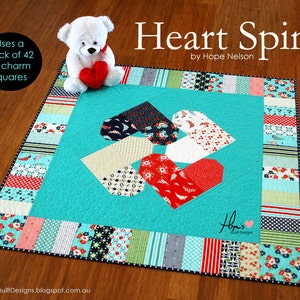 May include: A turquoise quilt with a heart-shaped design in the center. The quilt is made with a variety of colorful fabrics, including red, white, blue, and green. The quilt is surrounded by a border of white fabric with a black polka dot pattern. The quilt is titled "Heart Spin" and is by Hope Nelson.