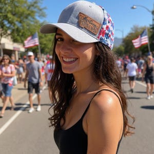 May include: Gray baseball cap with a leather Montana patch. The cap has a floral pattern in red, white, and blue on the back panel. The person in the image is smiling.