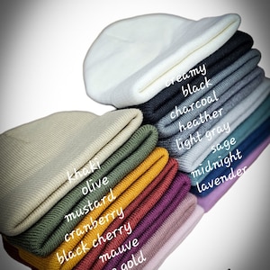 May include: A stack of 14 beanie hats in various colors, including olive, mustard, cranberry, black cherry, mauve, rose gold, creamy, black, charcoal, heather, light gray, sage, midnight, and lavender.