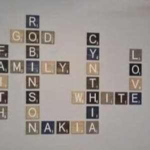 May include: A wall display of square wooden tiles arranged like a crossword puzzle. The tiles feature letters and small numerical values in the corners. The words spelled out include Robinson, Cynthia, White, Family, Faith, Love, and Nakia.