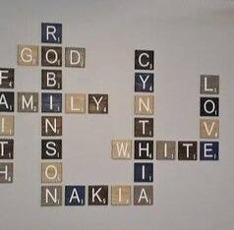 May include: A wall display of square wooden tiles arranged like a crossword puzzle. The tiles feature letters and small numerical values in the corners. The words spelled out include Robinson, Cynthia, White, Family, Faith, Love, and Nakia.