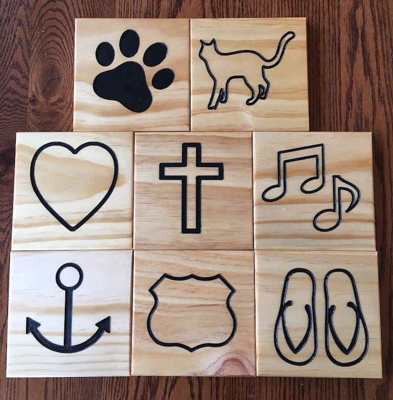 May include: Eight square wooden tiles featuring black engraved icons including a paw print, a cat silhouette, a heart, a cross, musical notes, an anchor, a shield-shaped emblem, and a pair of flip-flops, all displaying natural wood grain.