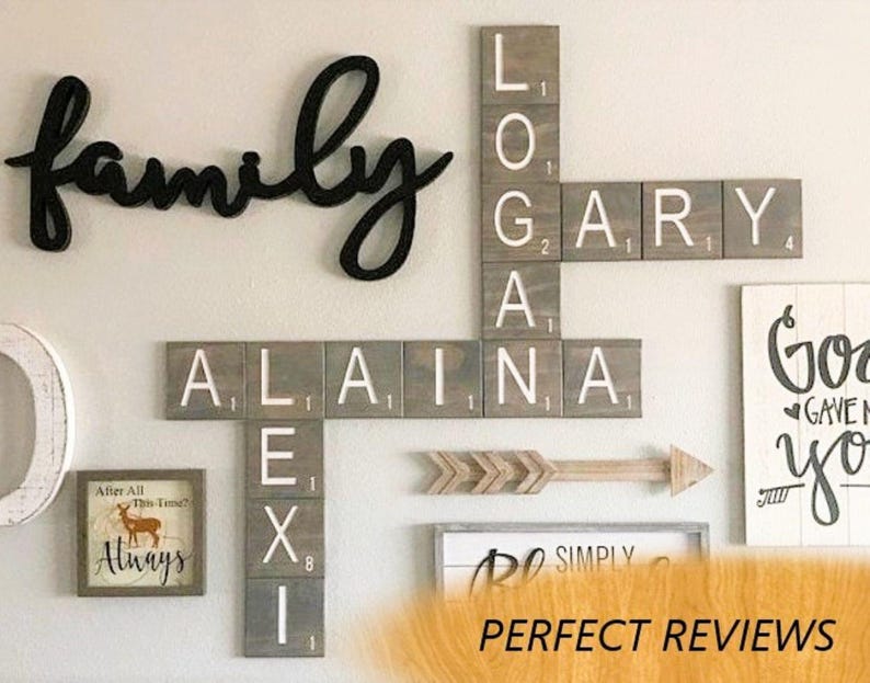 May include: A wall display featuring wooden tiles arranged like a crossword puzzle with the names LOGAN, GARY, ALAINA, and LEXI. The tiles are grey with white letters and small numerical values. A black cursive word family is mounted above the tiles.