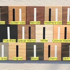 May include: A collection of fourteen square wooden samples arranged in three rows, each featuring a vertical stripe. The labels include Espresso, Golden Oak, Red Oak, Weatherd Oak, Honey, True Black, Special Walnut, White, Colonial Maple, Classic Gray, Original, Ebony, Cherry, and Dark Walnut.