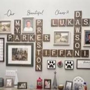 May include: A wall display featuring wooden letter tiles arranged like a crossword puzzle spelling names including Parker, Preston, Lukas, Dawson, and Tiffani, interspersed with various framed photographs, paw print art, and the text Our Beautiful Chaos.