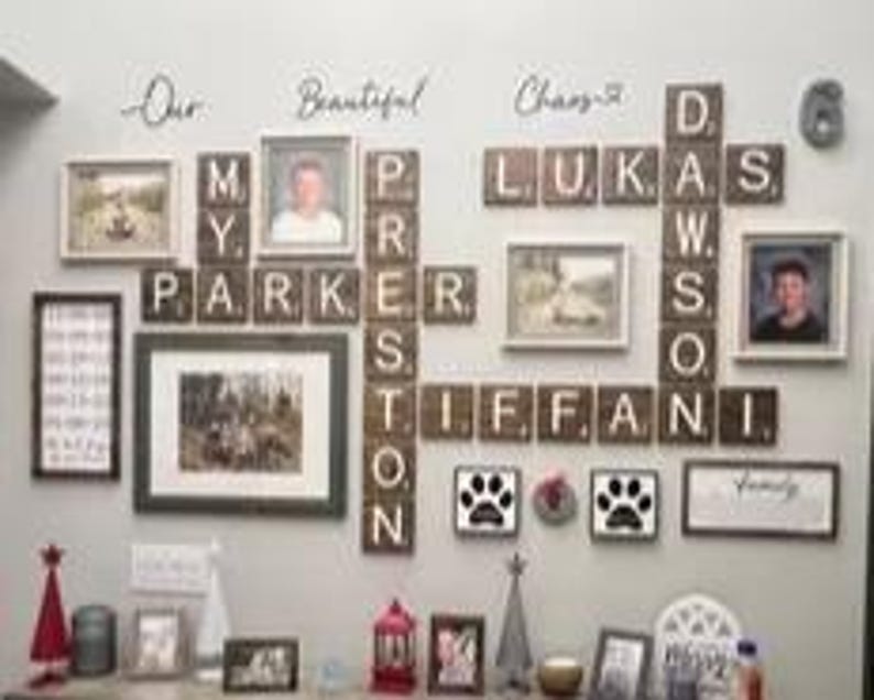 May include: A wall display featuring wooden letter tiles arranged like a crossword puzzle spelling names including Parker, Preston, Lukas, Dawson, and Tiffani, interspersed with various framed photographs, paw print art, and the text Our Beautiful Chaos.