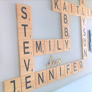 May include: A wall-mounted display of large, square wooden tiles resembling a board game, featuring black letters and numbers. The tiles are arranged in a crossword pattern to spell out the names Steve, Emily, Kaitlin, Allyson, and Jennifer, with the word love in script.
