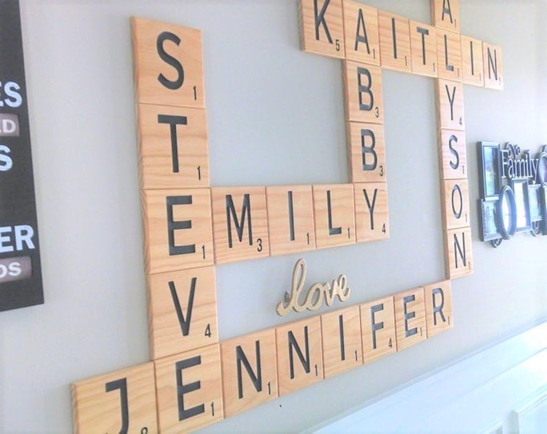 May include: A wall-mounted display of large, square wooden tiles resembling a board game, featuring black letters and numbers. The tiles are arranged in a crossword pattern to spell out the names Steve, Emily, Kaitlin, Allyson, and Jennifer, with the word love in script.
