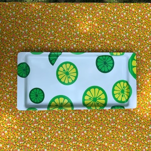May include: A rectangular white serving tray with a lime slice pattern in shades of green and yellow. The tray is set on a yellow floral patterned tablecloth.