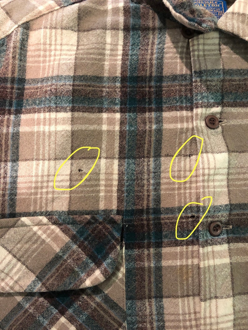 May include: Close-up of a button-down flannel shirt with a plaid pattern in shades of brown, teal, and cream. The shirt has a chest pocket and brown buttons. The fabric appears to be a soft, woven material.