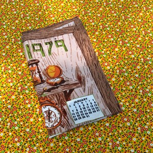 May include: A vintage calendar featuring the year 1979 in green lettering. The calendar has a wood-grain design with illustrations of an hourglass, compass, and a small table. The January calendar is visible. The background is a yellow floral pattern.