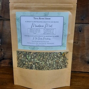 May include: A brown paper bag with a clear window, filled with dried herbs. The label reads "Teva Rose Herbs Mountain Mint" and lists ingredients and instructions. The bag contains 2.75 oz (78 gm) of tea.