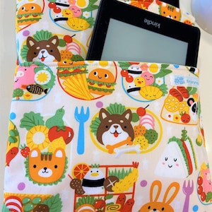 May include: A beige fabric pouch with a colorful print of cartoon animals and food. The pouch has a pocket on the front that can hold a Kindle e-reader. The text "Kindle" is visible on the e-reader.
