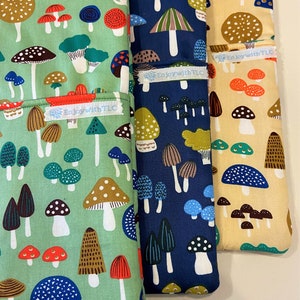 May include: Three fabric pouches with a mushroom pattern. The pouches are in green, blue, and yellow with the text "Enjoy with TLC" on each pouch.