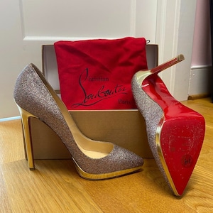 May include: Glittery high-heeled pumps with gold accents and signature red soles. The shoes are displayed with a red dust bag and a box. The brand name "Christian Louboutin Paris" is visible on the dust bag.