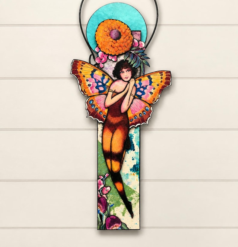 May include: A vertical wall hanging featuring a central figure with large, colorful butterfly wings in shades of orange, pink, and yellow. The figure is positioned against a rectangular panel with a teal circular accent, orange flower, and floral details.