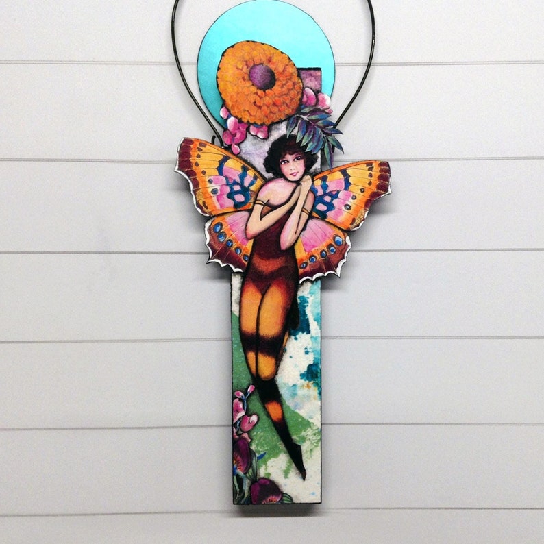 May include: A colorful wooden wall hanging featuring a whimsical fairy with butterfly wings, surrounded by flowers and a blue circle.