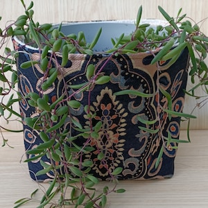 May include: A black and gold patterned fabric planter with a green succulent plant growing out of it.