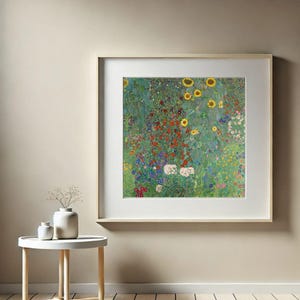 Puede incluir: Una impresi&oacute;n enmarcada de una colorida escena de jard&iacute;n, con girasoles y varias otras flores en tonos rojos, amarillos, blancos y azules. La obra de arte se exhibe en una pared beige, con una peque&ntilde;a mesa blanca y jarrones en primer plano.