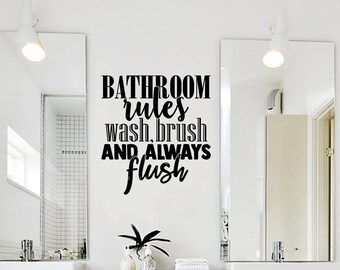以下が含まれることがあります： 太字のサンセリフ体と筆記体を組み合わせた「BATHROOM rules wash, brush AND ALWAYS flush」というテキストの黒いビニール製ウォールステッカー。ステッカーは、洗面台の上の2つの長方形の鏡の間の白い壁に貼られています。
