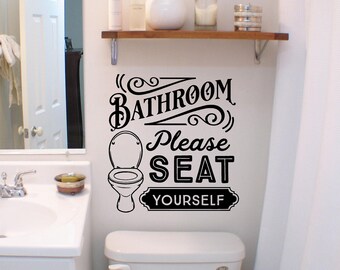 以下が含まれることがあります： トイレの上のバスルームの壁に貼られた黒いビニール製のウォールステッカー。ステッカーには、トイレのグラフィックイラストと、装飾的なフォントと渦巻き模様でデザインされた「BATHROOM Please SEAT YOURSELF」という定型化されたテキストが含まれています。