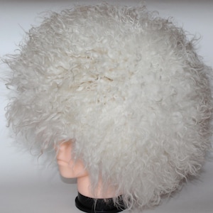 Può includere: Un cappello bianco e soffice con una trama fitta e riccia. Il cappello è rotondo e copre la testa, con un aspetto pieno e voluminoso. Il cappello è realizzato in un materiale morbido, forse simile alla pelliccia.