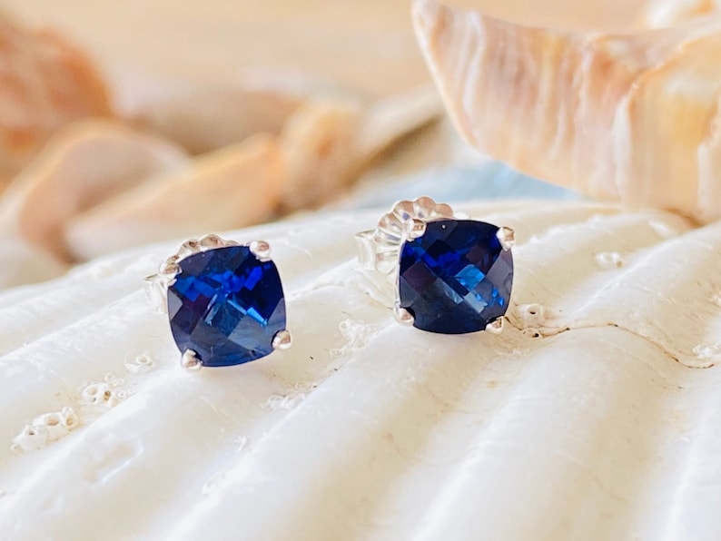 Puede incluir: Un par de pendientes de bot&oacute;n de plata con una piedra preciosa cuadrada azul oscuro en cada uno.