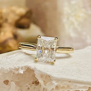 May include: A gold engagement ring featuring a large, clear, square-shaped diamond.