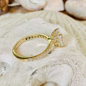 Pode incluir: Um anel de noivado de ouro com uma grande pedra central oval transparente e uma banda de diamantes menores.