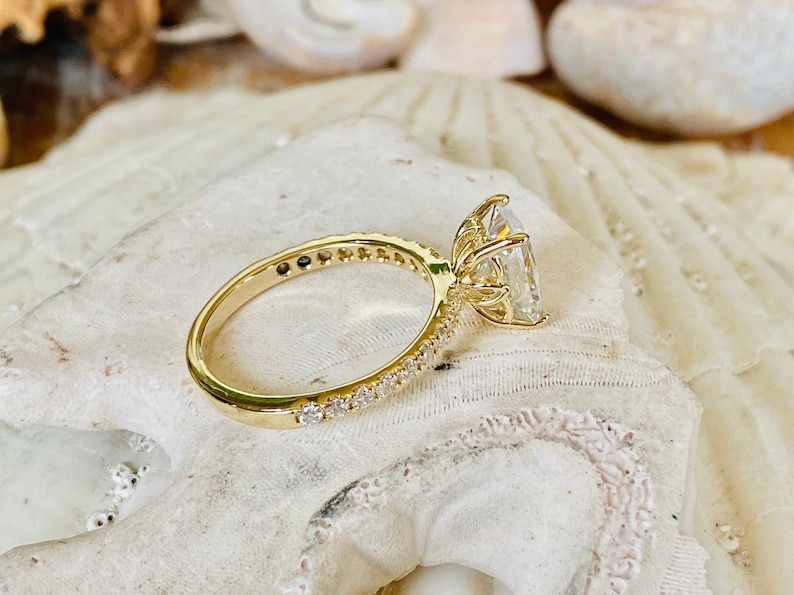 Pode incluir: Um anel de noivado de ouro com uma grande pedra central oval transparente e uma banda de diamantes menores.