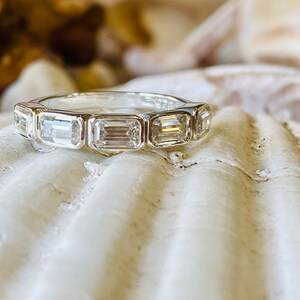 May include: A silver band ring with seven emerald-cut diamonds set in a row.