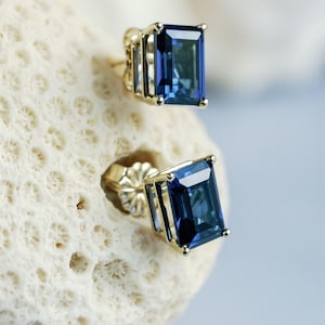 Puede incluir: Un par de pendientes de oro con piedras preciosas azules. Las piedras preciosas son de corte esmeralda y tienen un color azul oscuro.