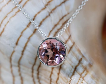 May include: A silver chain necklace with a round, bezel-set pink gemstone pendant.